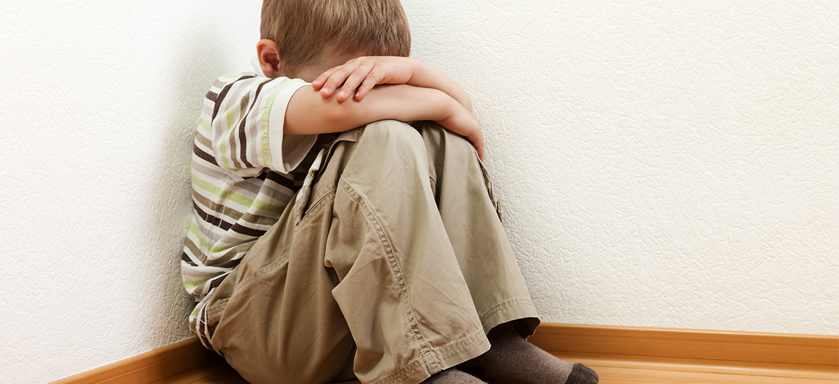 Child sitting in corner with head down