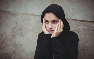 Anxious teenage girl in black hooded jacket standing with hand on face